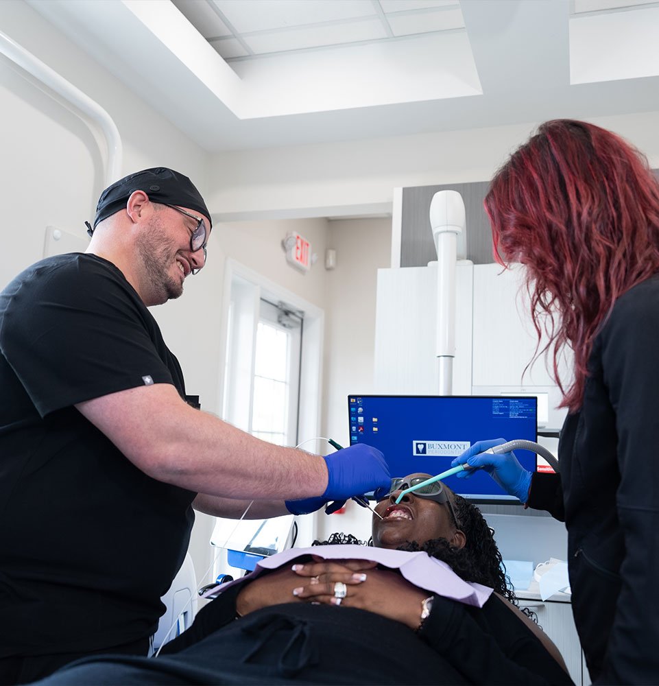 doctor and staff member performing dental treatment with patient